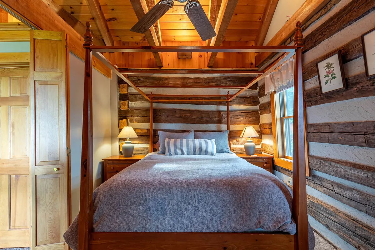 This image displays a tranquil king bedroom featuring a four-poster bed with natural wood walls and lamps on the nightstands. The window allows natural light to gently fill the room, creating a peaceful sleeping environment.