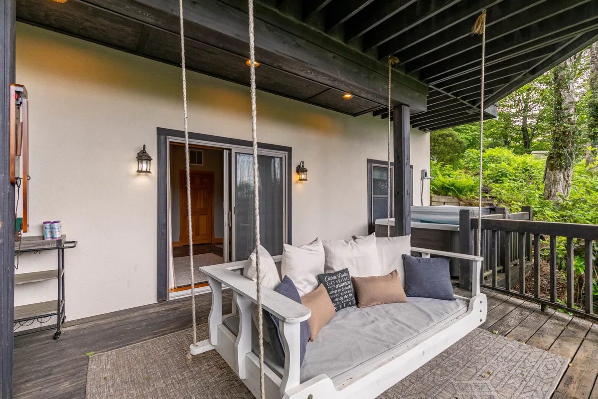 A peaceful exterior scene displays a swing bench complemented by lanterns and sliding doors leading inside the house. The area is shaded by trees, and the swing provides a comfortable spot to relax while taking in the natural beauty.