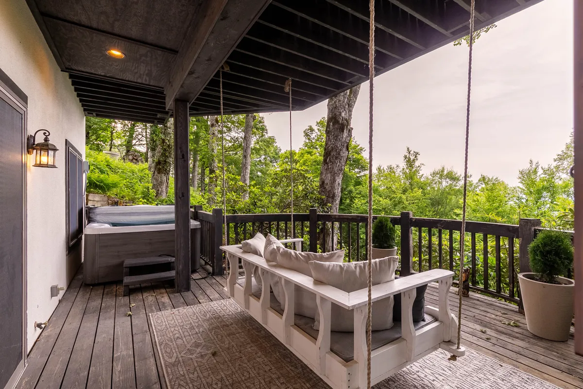 This exterior image features a bed-style swing and a hot tub set on the lower deck, surrounded by greenery. The atmosphere is calm and inviting, ideal for unwinding outdoors or entertaining guests.