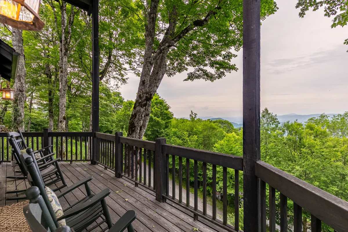This image features a pair of classic rocking chairs positioned on a wooden deck, overlooking lush greenery and a sweeping mountain view. The tranquil setting is accentuated by the late afternoon light and the closeness of nature, inviting relaxation and quiet contemplation.