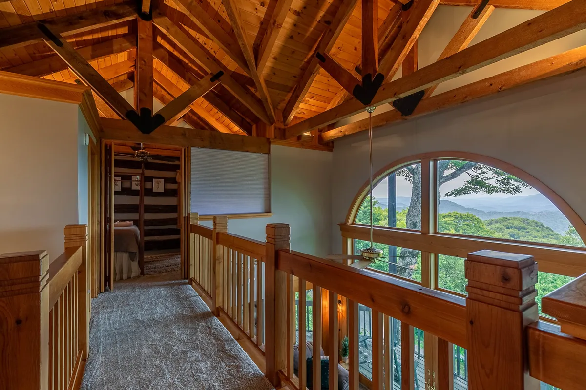 A cozy interior landing features an arched window offering expansive views of the surrounding mountains, with exposed wooden beams and soft lighting creating a warm atmosphere. The space invites relaxation and quiet contemplation while maintaining a strong connection to the outdoors.