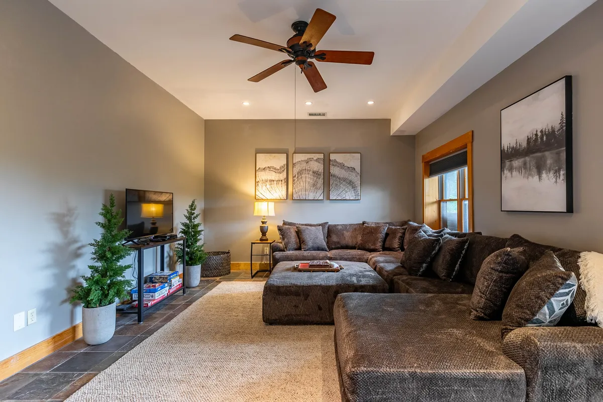 This image shows a cozy living space with a large sectional sofa, artwork on the wall, and a TV stand adorned with plants. The space is inviting, perfect for relaxing, watching TV, or gathering with family and friends.