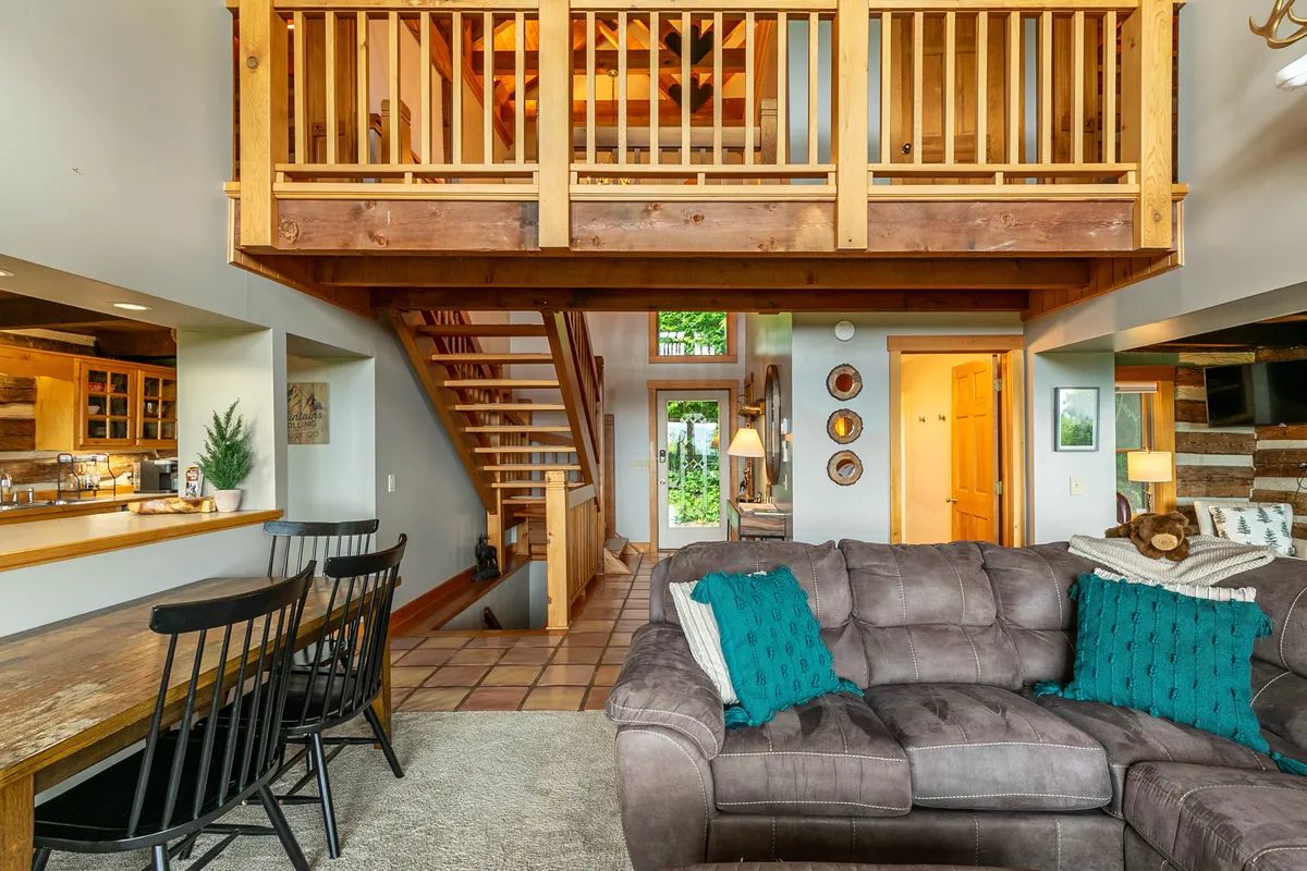 A warm, inviting interior space featuring a wooden staircase, a comfortable living room couch, and a dining area. The scene exudes coziness, with clear opportunities for gathering around the fire, relaxing, or sharing intimate moments with friends and loved ones.