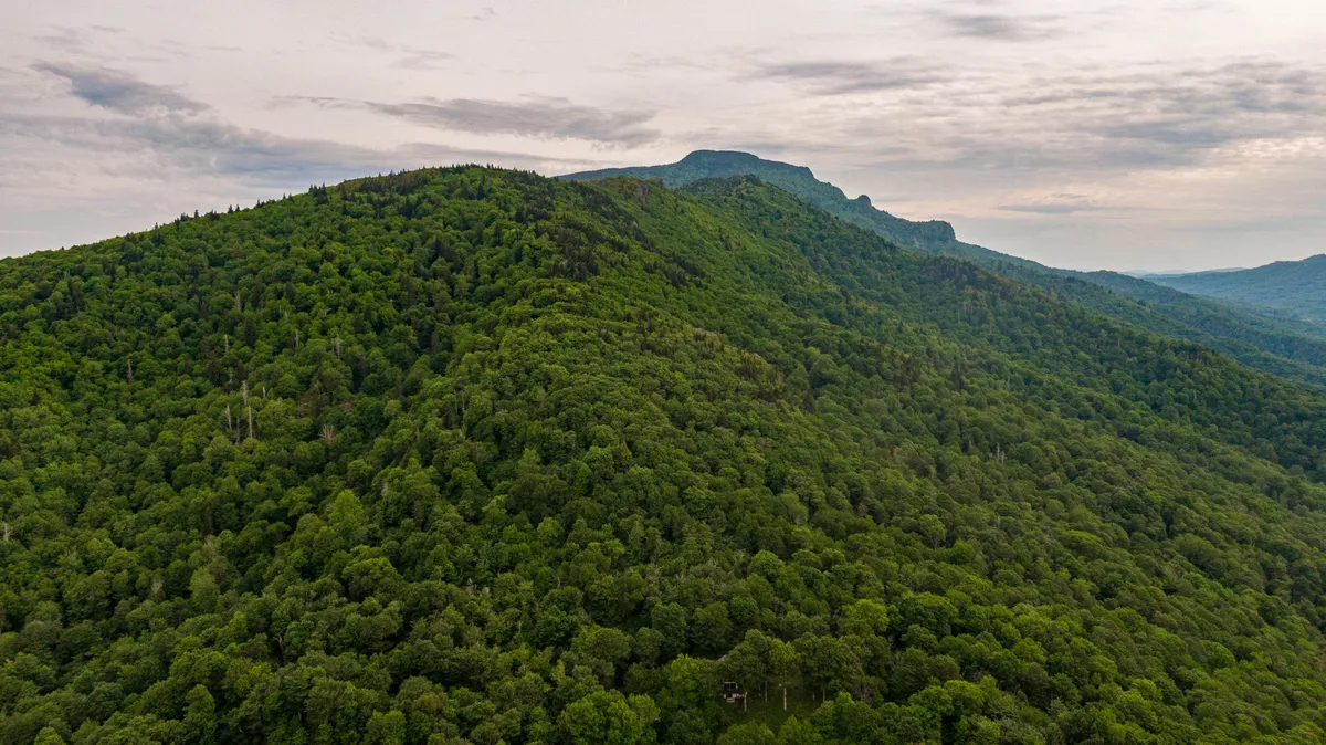 A sweeping view of lush green mountains with a distant peak under a cloudy sky. The natural landscape is inviting, tranquil, and hints at the outdoor adventures available nearby, such as hiking, birdwatching, and stargazing.