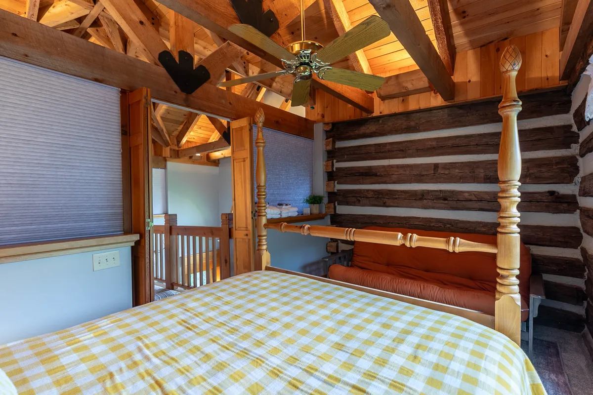 Here, a queen bedroom features a four-poster bed, exposed wooden beams, and a cozy sofa with a checkered bedspread. The space feels open yet private, with sunlight filtering in, reinforcing the sense of a treehouse hideaway.
